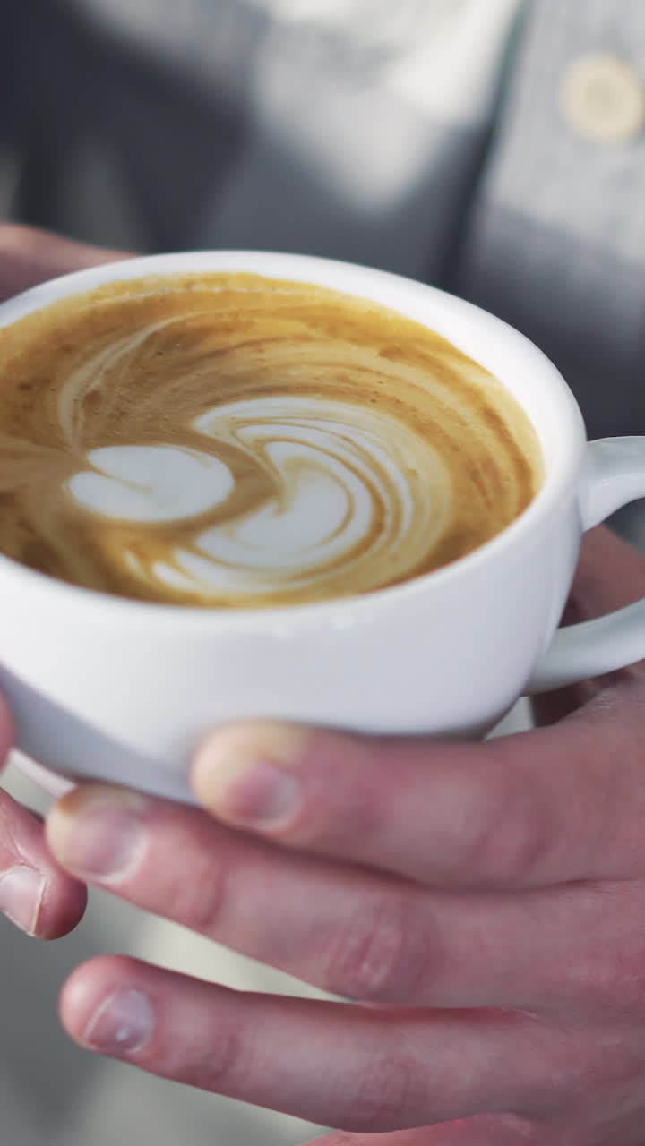 Professional barista pouring milk foam over coffee into white cup creating perfect cappuccino and making a nice pattern. Vertical video.