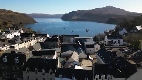 Volando-Sobre-Los-Edificios-Y-Sobre-El-Tranquilo-Puerto-De-Portree,-Isla-De-Skye,-Escocia