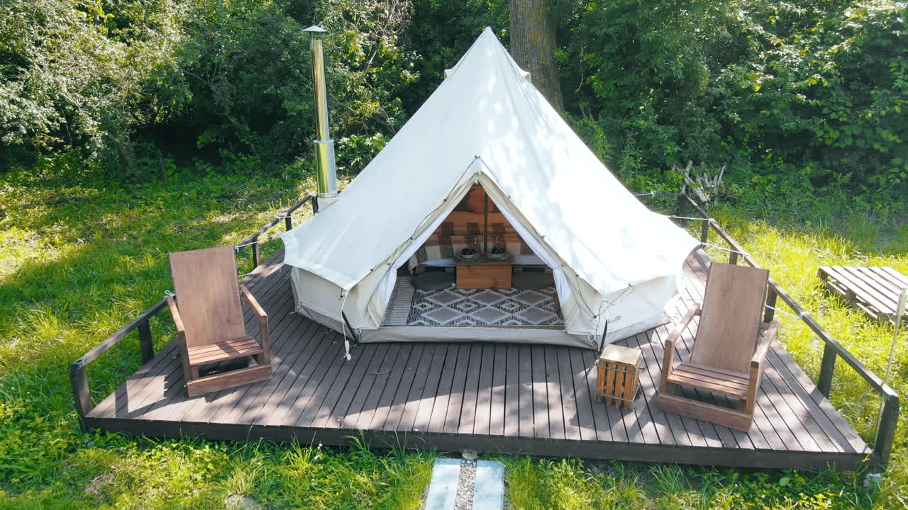 Interior of a glamping tent with chairs outside, nature, green grass and trees, trail
