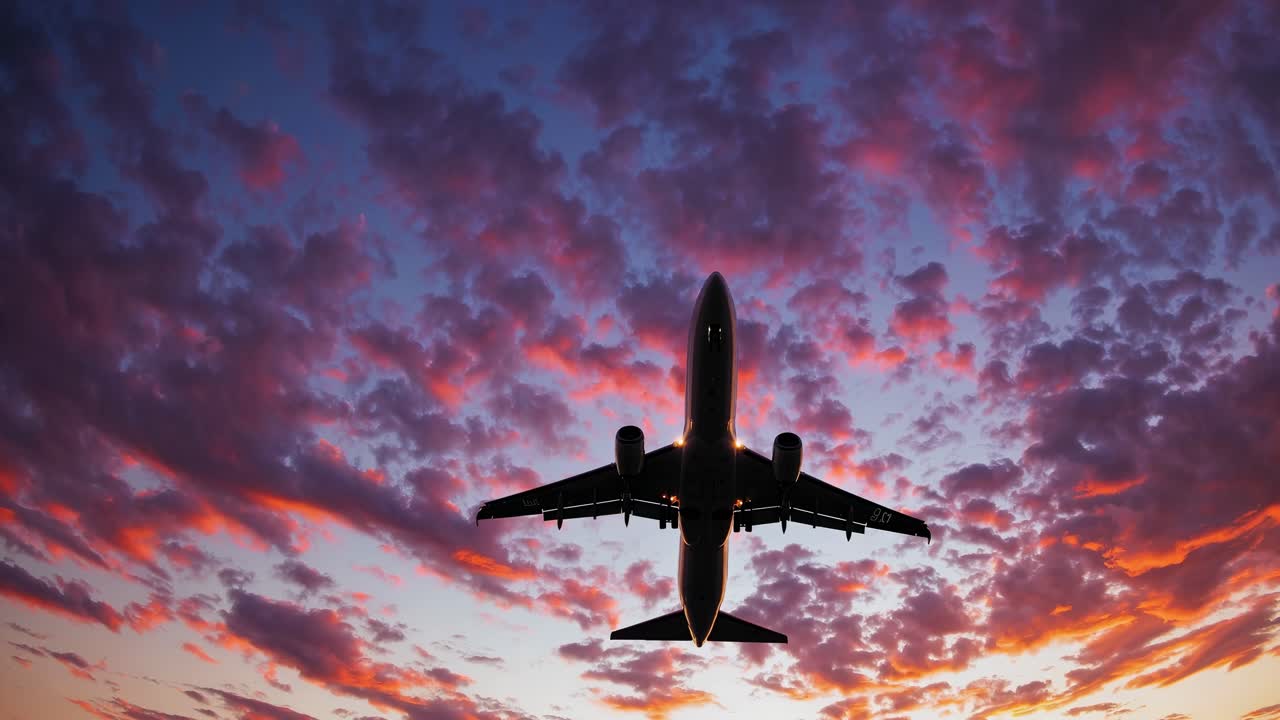 Dramatic low-angle shot of an airplane silhouetted against a vibrant sunset sky