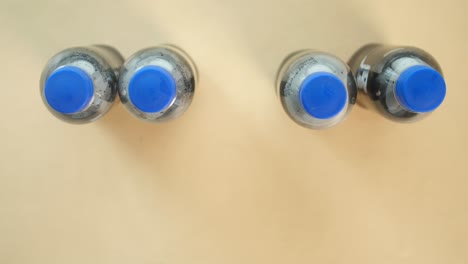 close up of four soda bottles with blue caps on a brown table