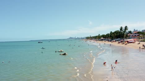 dolly in aerial shot of bessa beach in the tropical capital joao pessoa, brazil in the state of paraiba with brazilians and tourists enjoying the ocean and fishing boats at shore on a summer day