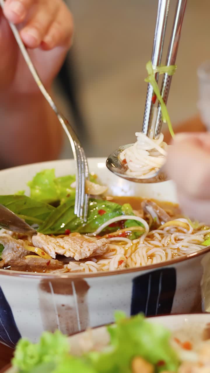 Cận cảnh đôi tay đang dùng đũa và muỗng để ăn món phở truyền thống Việt Nam trong một tô.