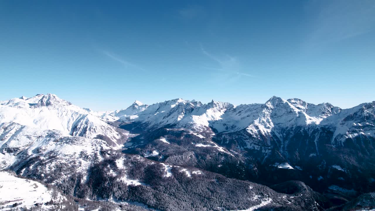 Aerial reveal of snow covered mountain landscape with forests on a sunny winter day in Alp Grum, Switzerland