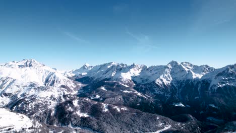 Aerial-reveal-of-snow-covered-mountain-landscape-with-forests-on-a-sunny-winter-day-in-Alp-Grum,-Switzerland