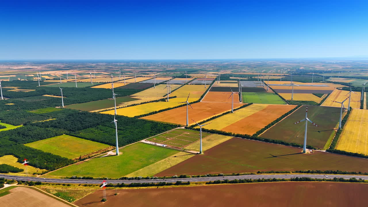Tall turbines in green fields. Vast rural landscape with wind turbines against a clear blue sky and vibrant fields stretching to the horizon