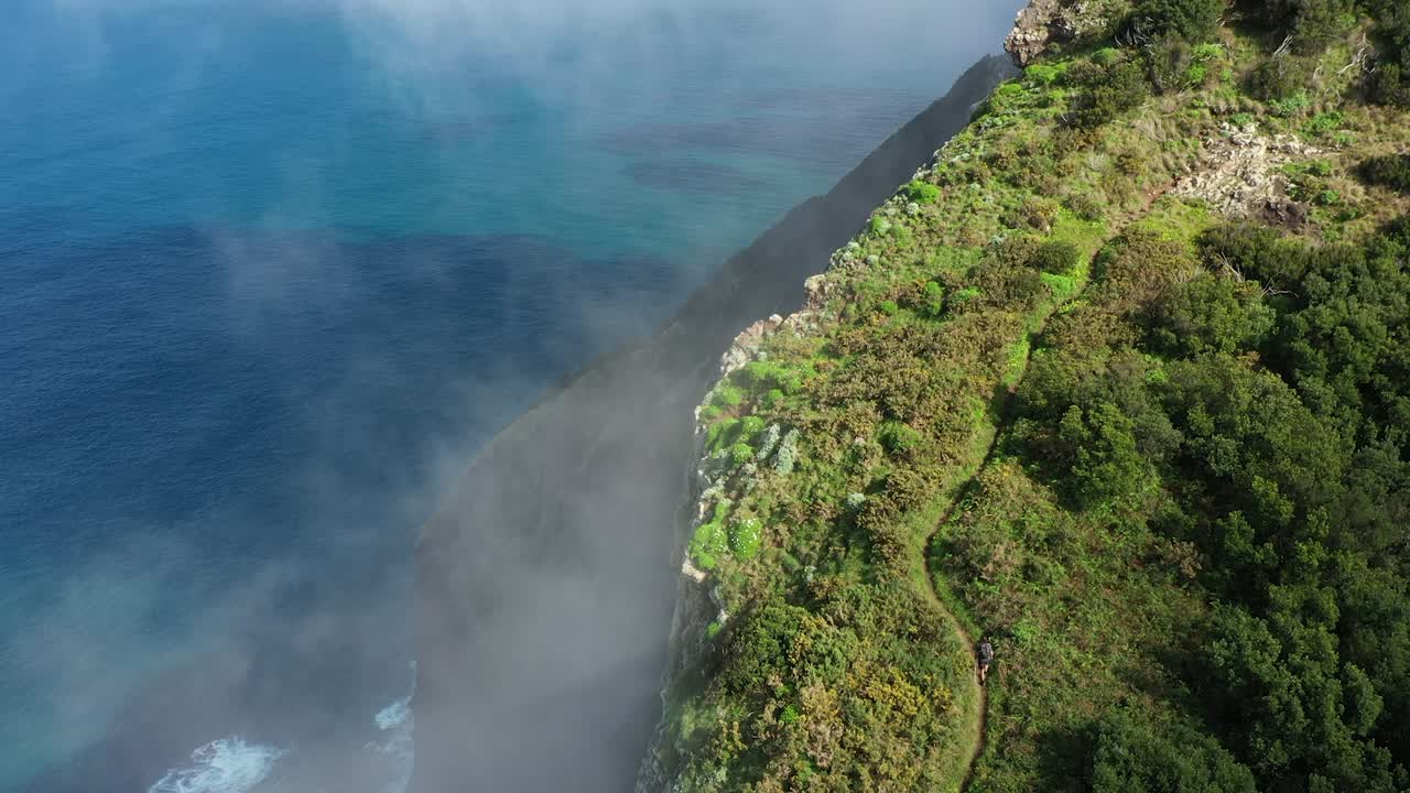 Drone shot going upwards of a young, fit and strong man hiking up Espigao Amorelo on Maderia during the summer