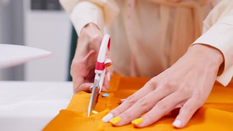 seamstress cutting orange fabric with scissors