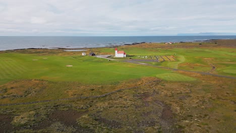 vista de paralaje, tranquilo pueblo islandés con campo de golf, iglesia con techo rojo y naturaleza verde