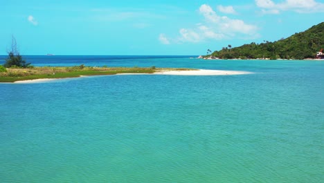 Peaceful-calm-turquoise-lagoon-with-tiny-island-in-the-middle-of-beautiful-bay-of-tropical-island-under-bright-sky-with-white-clouds,-Thailand