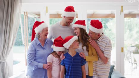 Portrait-of-family-wearing-santa-hats-smiling-and-standing-together-in-the-living-room-at-home