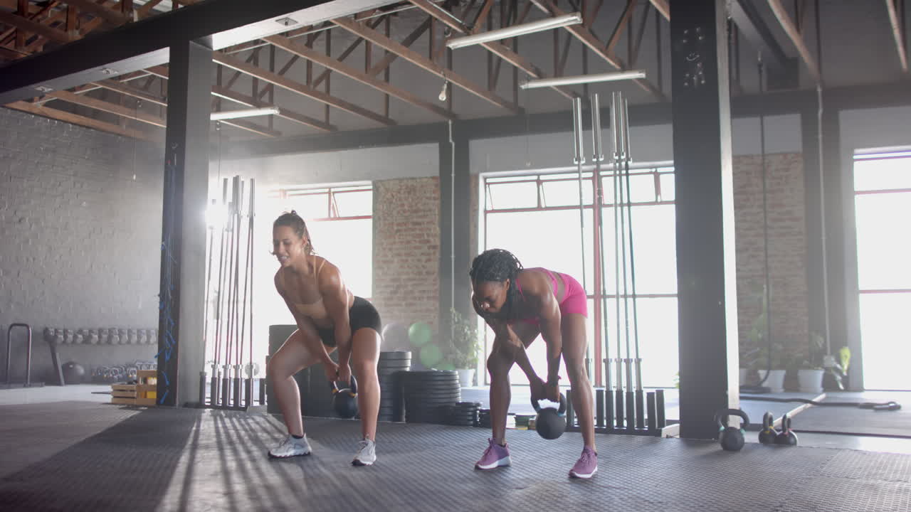 Exercising with kettlebells, two women stretching in gym, focusing on fitness