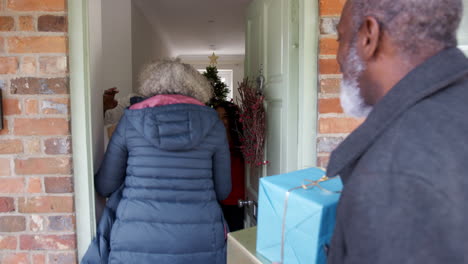 grandparents being greeted by mother and daughter as they arrive for visit on christmas day with gifts