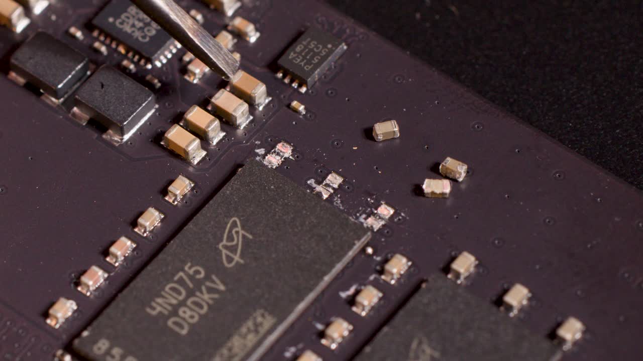 Close-up of metal tool manipulating microchip components on circuit board under controlled studio lighting