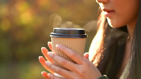 a serene moment: a young woman enjoys a warm beverage in nature as sunlight filters through the trees, filling the scene with a cozy glow and a sense of peace