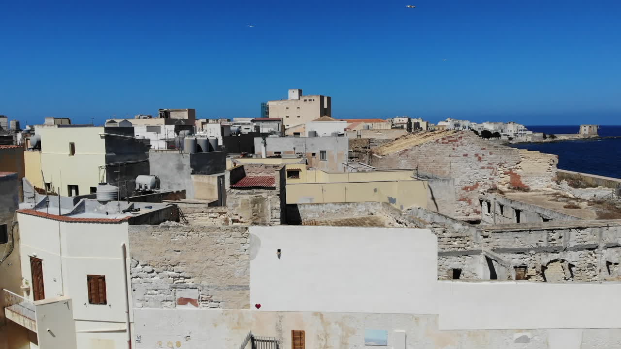 Ascesa di un drone sui tetti di Trapani, in Sicilia, che rivela il porto e la costa mediterranea, con gabbiani che volano naturalmente nell'inquadratura.