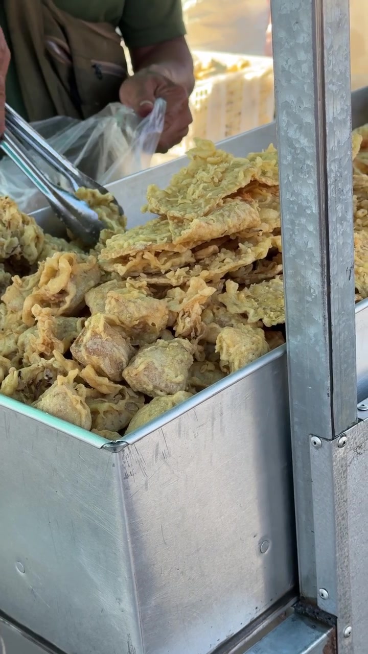 Venditore di street food che serve spuntini fritti da un contenitore di metallo.