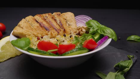 extreme-close-up-dolly-shot-of-a-bowl-of-delicious-fresh-produce,-vegan-meat,-sitting-on-a-slate-plate-with-a-lemon-wedge-and-lettuce-garnish,-rotating-slowly