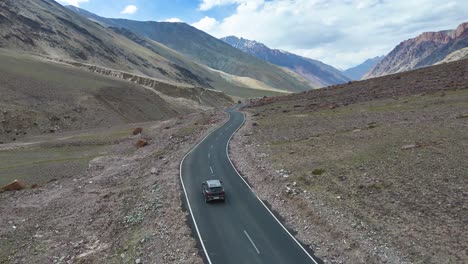 aerial drone shot showing a car cruising along a straight road with towering peaks in the background.