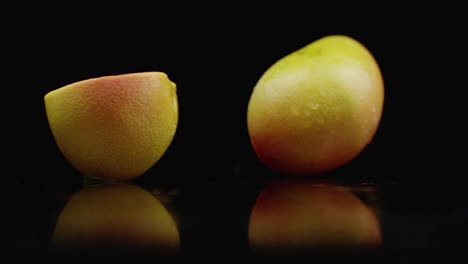 slow motion. juicy grapefruit with drops and breaks into 2 slices with splashes on a glass table with reflection on a dark background.