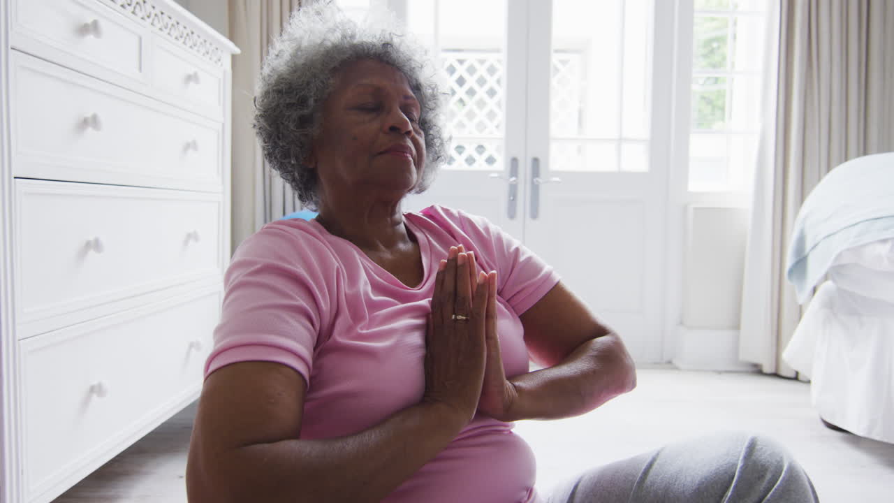 Donna afroamericana anziana che pratica yoga in camera da letto a casa
