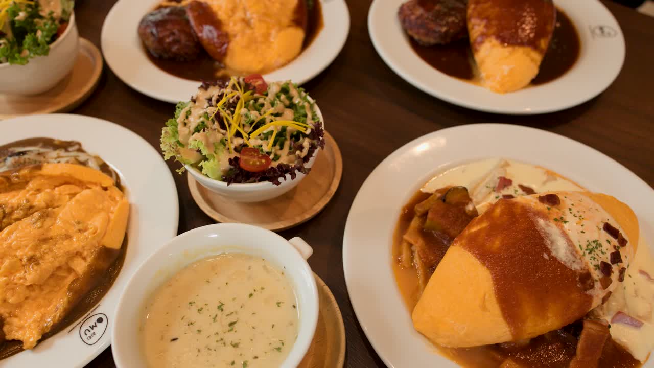 Overhead pan of Japanese omelette rice, creamy soup, salad, and hamburger steak in warm lighting