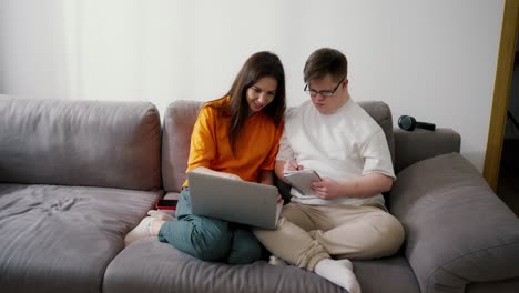 A-guy-with-down-syndrome-writing-notes-from-laptop-at-home-together-with-teacher-or-sister