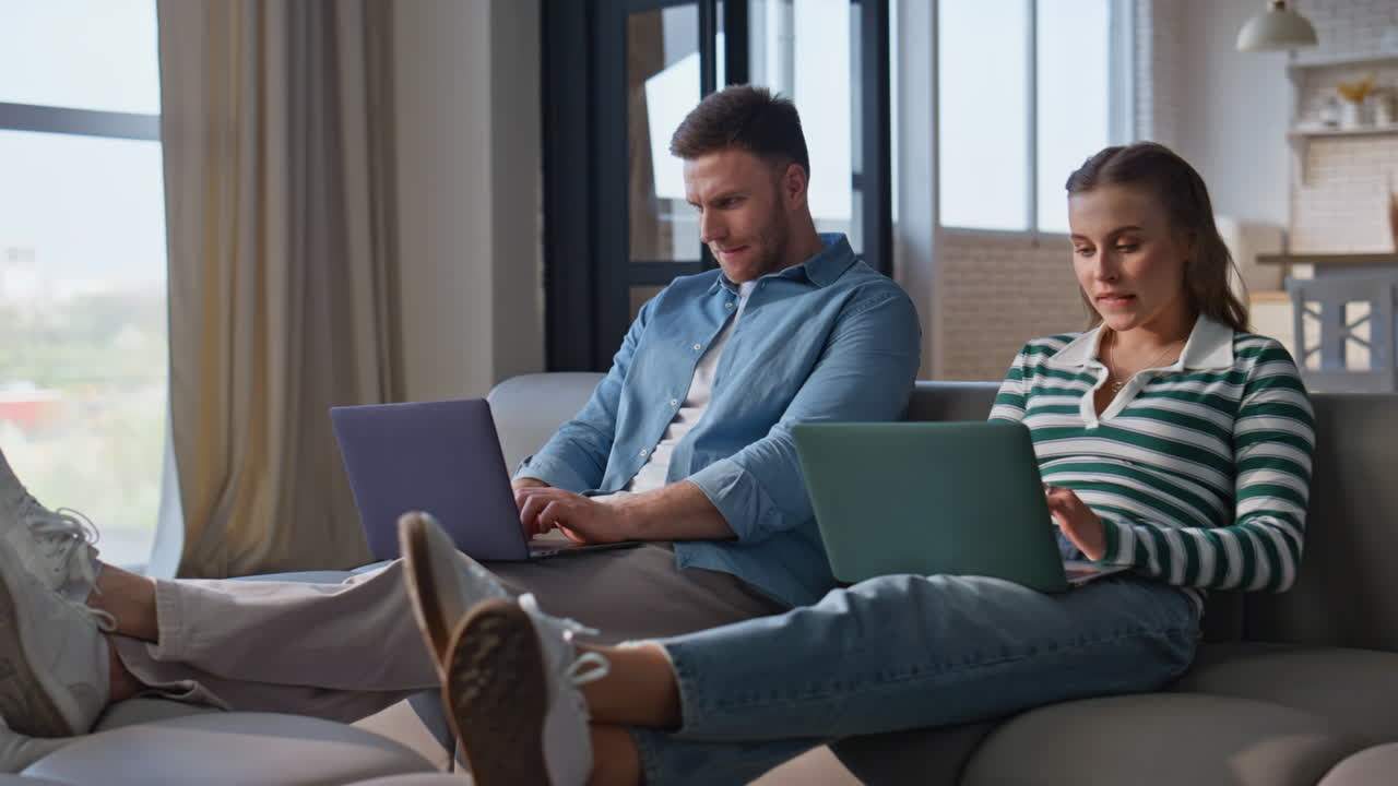 Focused couple working laptops at living room interior. Happy man looking woman