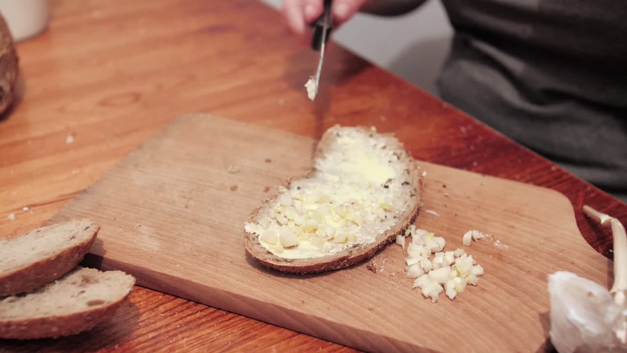 Woman's hands puts garlic on slice of bread with butter