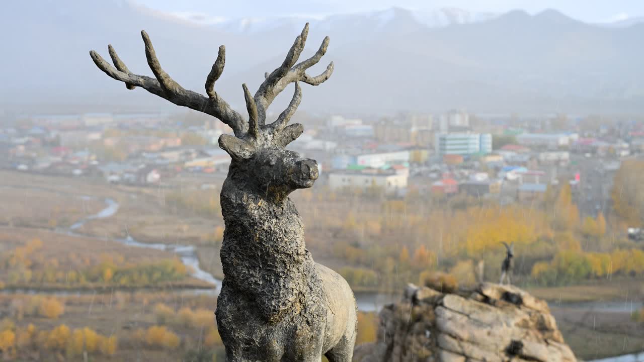 An atmospheric, scenic view from a deer monument as light snow falls on Uliastai, Mongolia. The hazy autumn landscape of the town and river valley stretches out below
