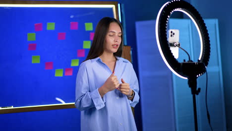 young woman creates online content. a young woman talks energetically while standing in front of a ring light, preparing for her online livestream or video