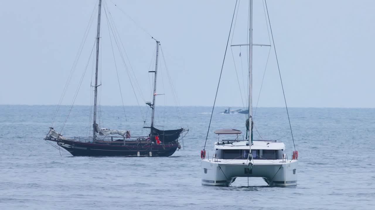 A sailboat and catamaran are seen side by side on a calm ocean.