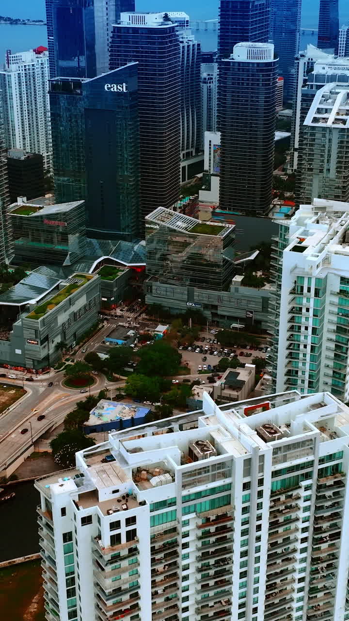 Approaching the tops of high-rise blocks of flats in the modern city downtown. Scenic view of Miami, Florida, USA on grey daytime. Vertical video