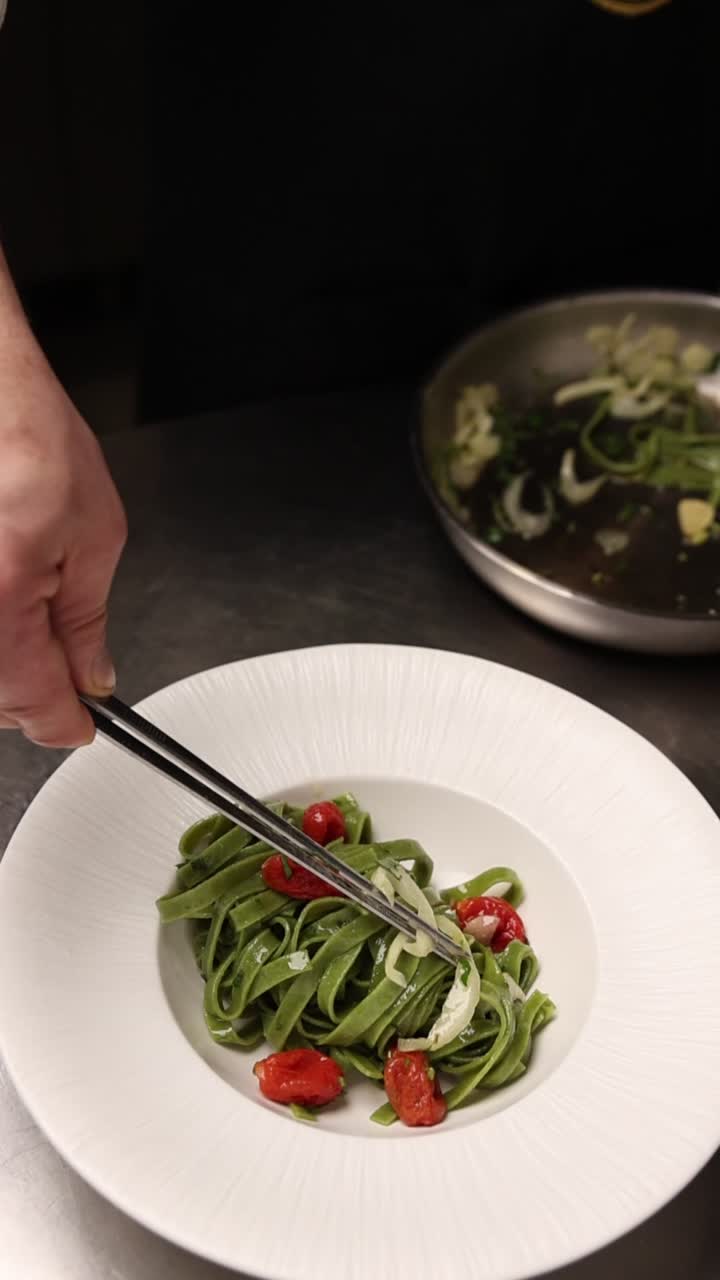 Chef Plating Green Pasta with Cherry Tomatoes and Onions in a Restaurant Kitchen