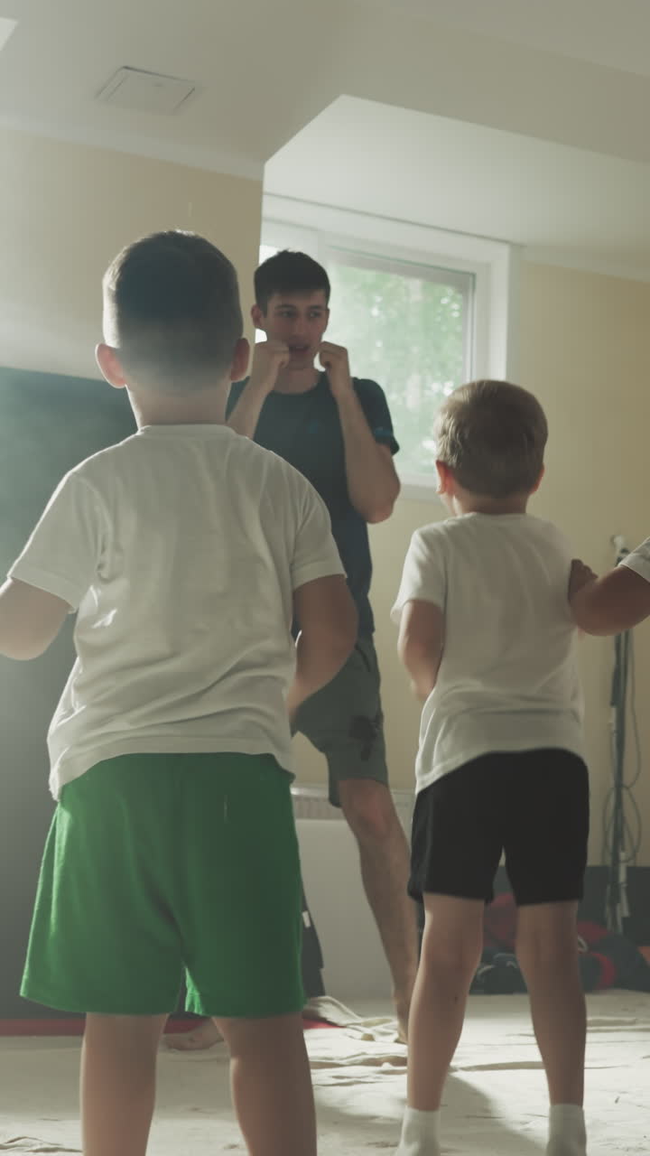 아이들은 무술 학교에서 강사와 함께 발로 뛰고 훈련합니다. 어린 아이들은 체육관에서 젊은 센세이와 함께 다리 타격을 연습합니다. 느린 동작. 전투 기법
