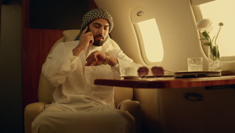 Smiling-businessman-talking-cellphone-on-luxury-airplane-in-muslim-clothing.