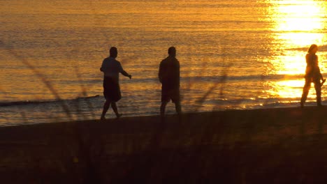 a woman and two men walking on beach at dawn, sunlight on water