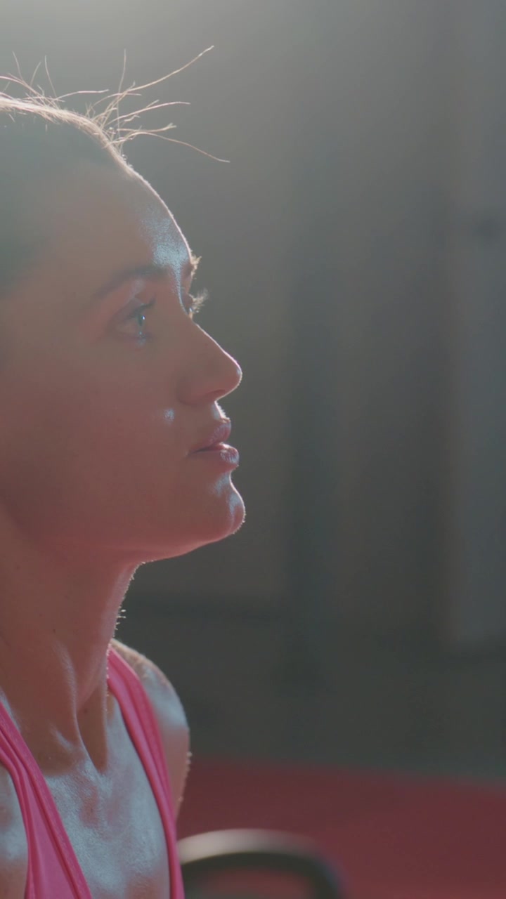 Athlete breathes heavily after lifting weights. Sweat glistens on her skin. Sunlight highlights her focused expression. She trains intensely in a gym. Perfect for fitness, motivation