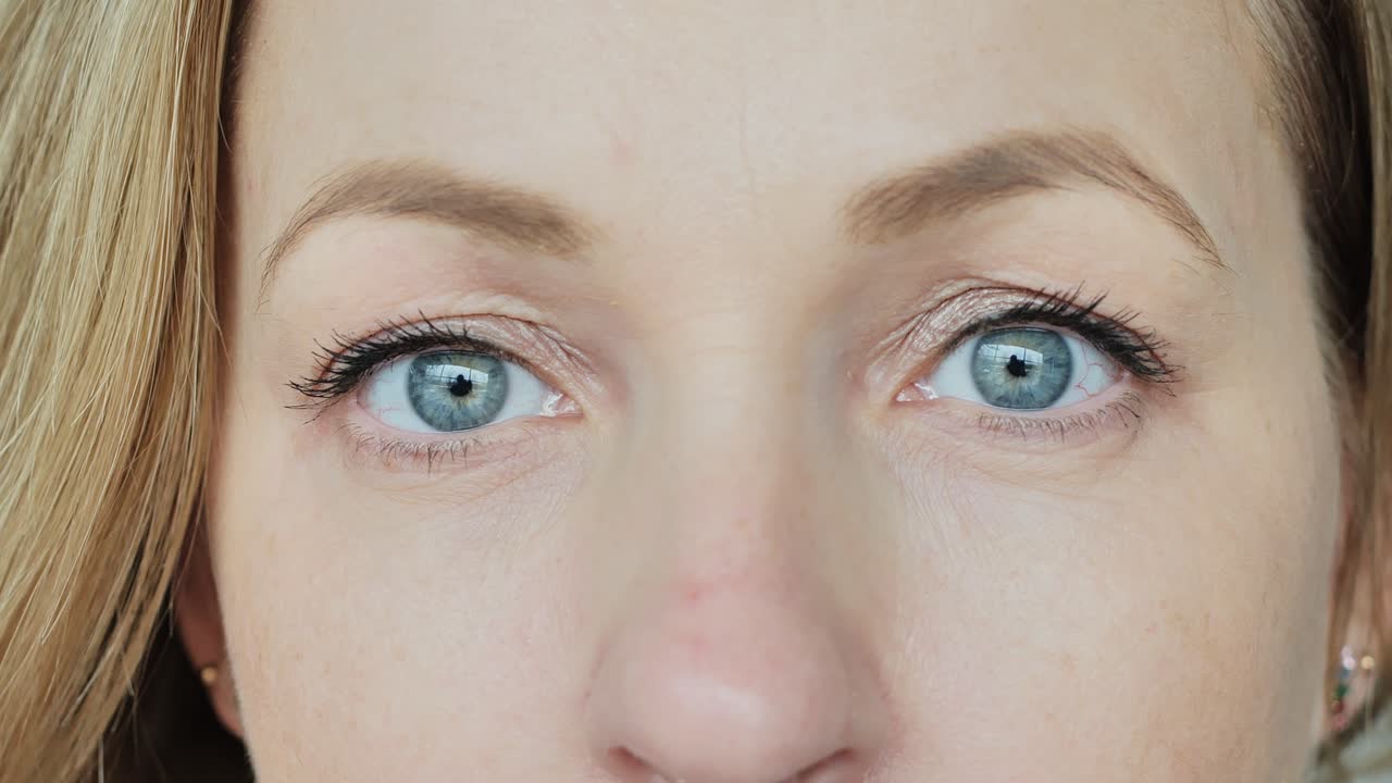 Extreme close-up of woman calm blue eyes looking forward with slow motion focus