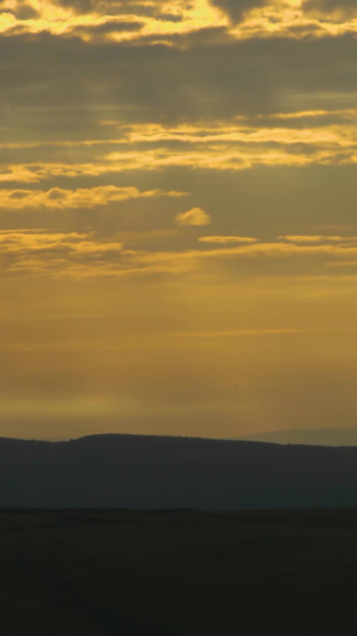 Vertical Video of Dramatic Sunrise Over Hill Landscape with Layers of Clouds with Dawn Lighting and Small Light Rays.