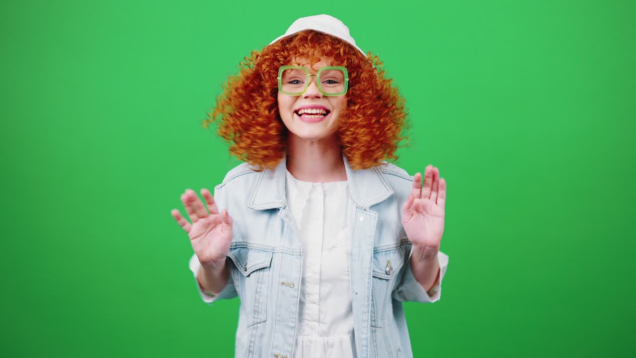 joven rubia linda mujer rizada con gafas y sombrero de panama mirando a la cámara, disfrutando de la reunión y agitando las manos