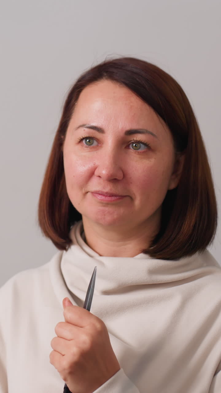 Instructor caucásico mostrando cómo usar las tijeras de forma segura en un estudio tranquilo y neutro, gesticulando para guiar sobre la punta y el mango, con expresión atenta, ambiente de lección práctica, manos mostrando una técnica segura