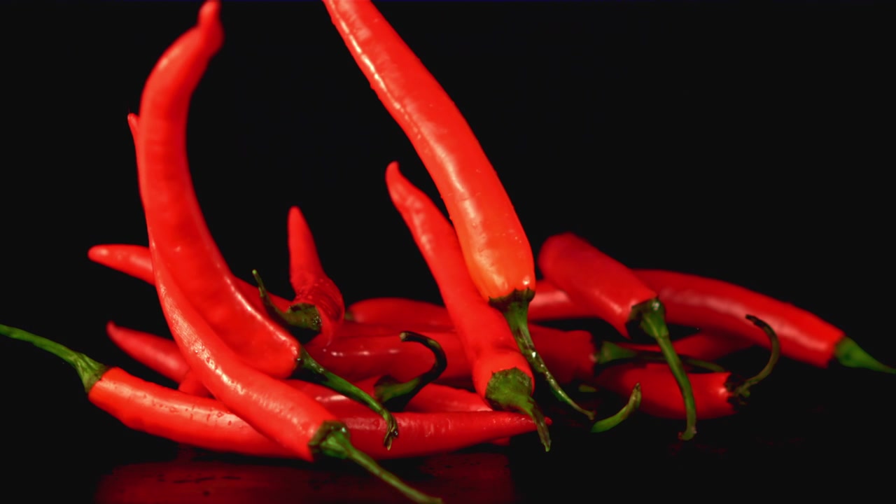 Red Chili Peppers Falling and Piling Up on a Black Background in Slow Motion