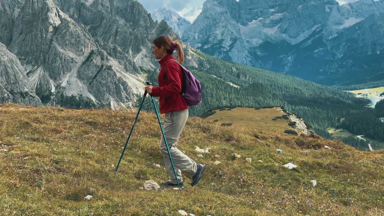 Female hiker walking along mountain trail, featuring iconic Cadini di Misurina rising dramatically against summer sky in scenic Dolomites landscape
