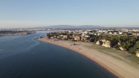 aerial view of praia grande beach coastline next to arade river in portugal on clear day with blue skies