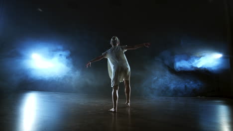 una escena dramática de ballet moderno una bailarina solitaria en un vestido blanco realiza pasos de baile usando coreografía moderna.