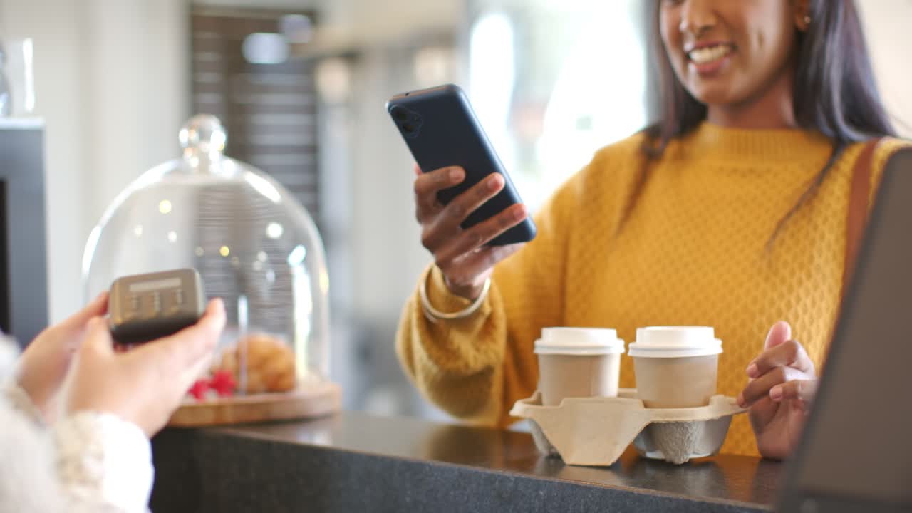as payment terminal extending at counter Indian woman scanning smartphone picking cups, copy space