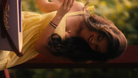 una hermosa modelo caucásica abre una caja de regalos sonriendo, sorprendida video vertical, con un vestido amarillo en el ambiente del jardín