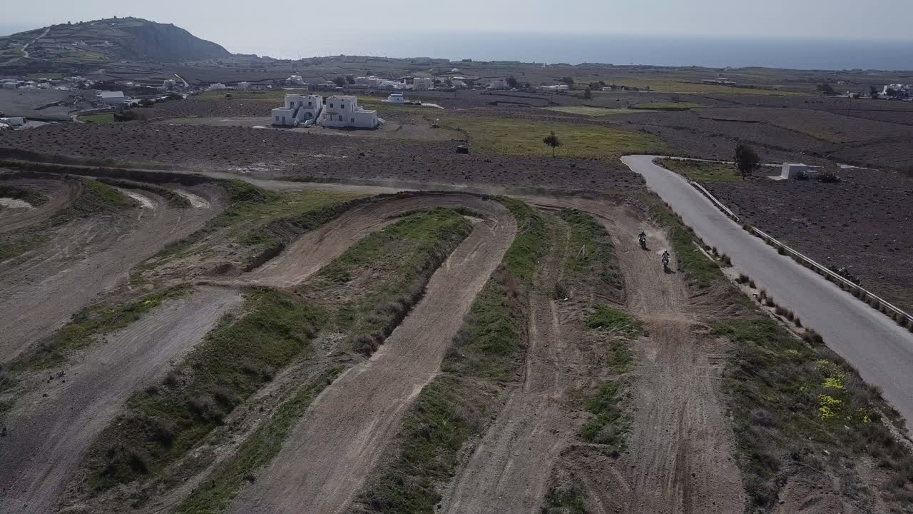 먼지가 많은 트랙에서 모터크로스 라이더의 드론 샷, 카메라 아래를 통과하기 위해 패닝