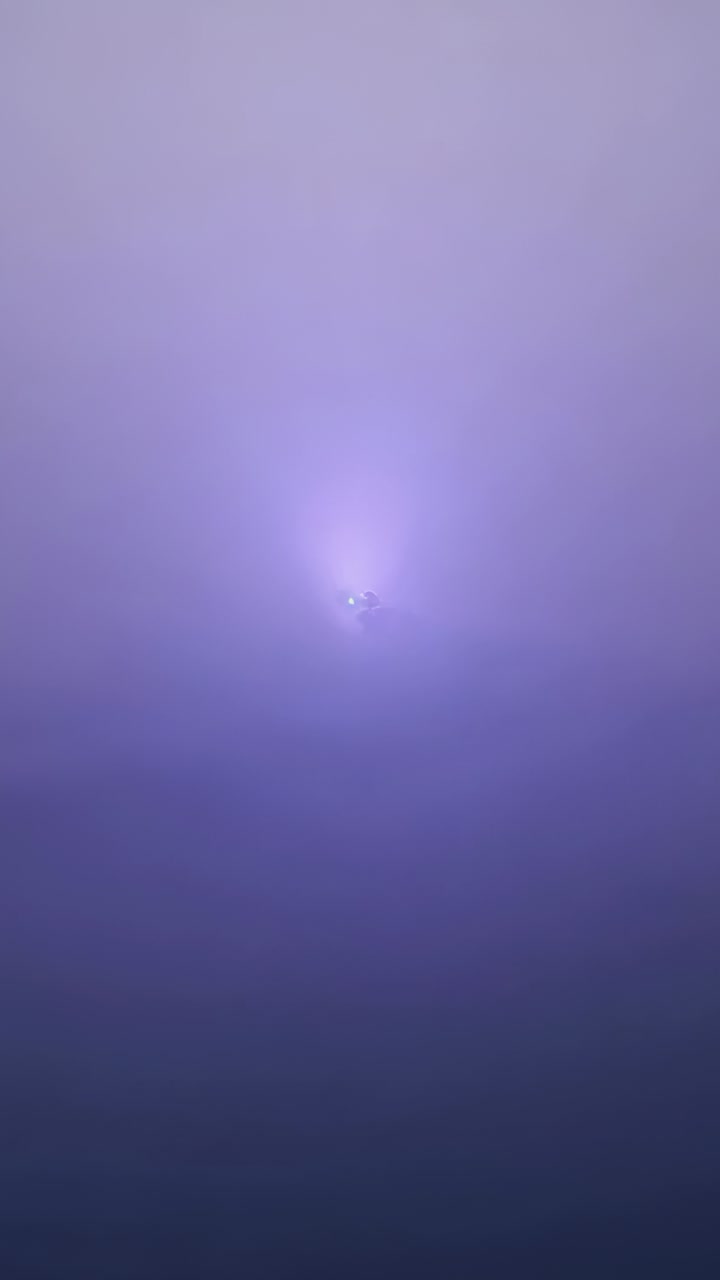 Vertical video: Appearing light point intensifying, sending flare over purple sky, cloud moving in